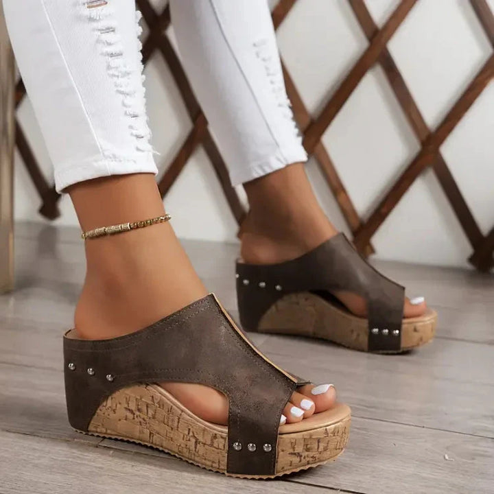 Braune Keilsandalen mit Nieten, getragen von Person in weißen, zerrissenen Jeans. Modische Sommerschuhe, ideal für Damenmode und Freizeitoutfits.