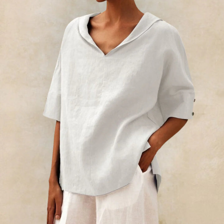 Frau trägt lockere, weiße Leinenbluse mit V-Ausschnitt und kurzen Ärmeln. Sommermode, minimalistischer Stil, elegante Damenbekleidung.
