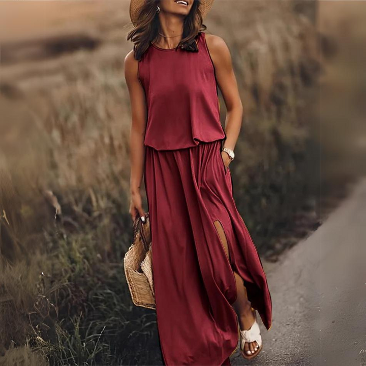 Frau in rotem Maxikleid mit Schlitz, Strohhut und Sandalen spaziert auf ländlichem Weg, trägt geflochtene Tasche. Sommermode, Freizeitkleidung.