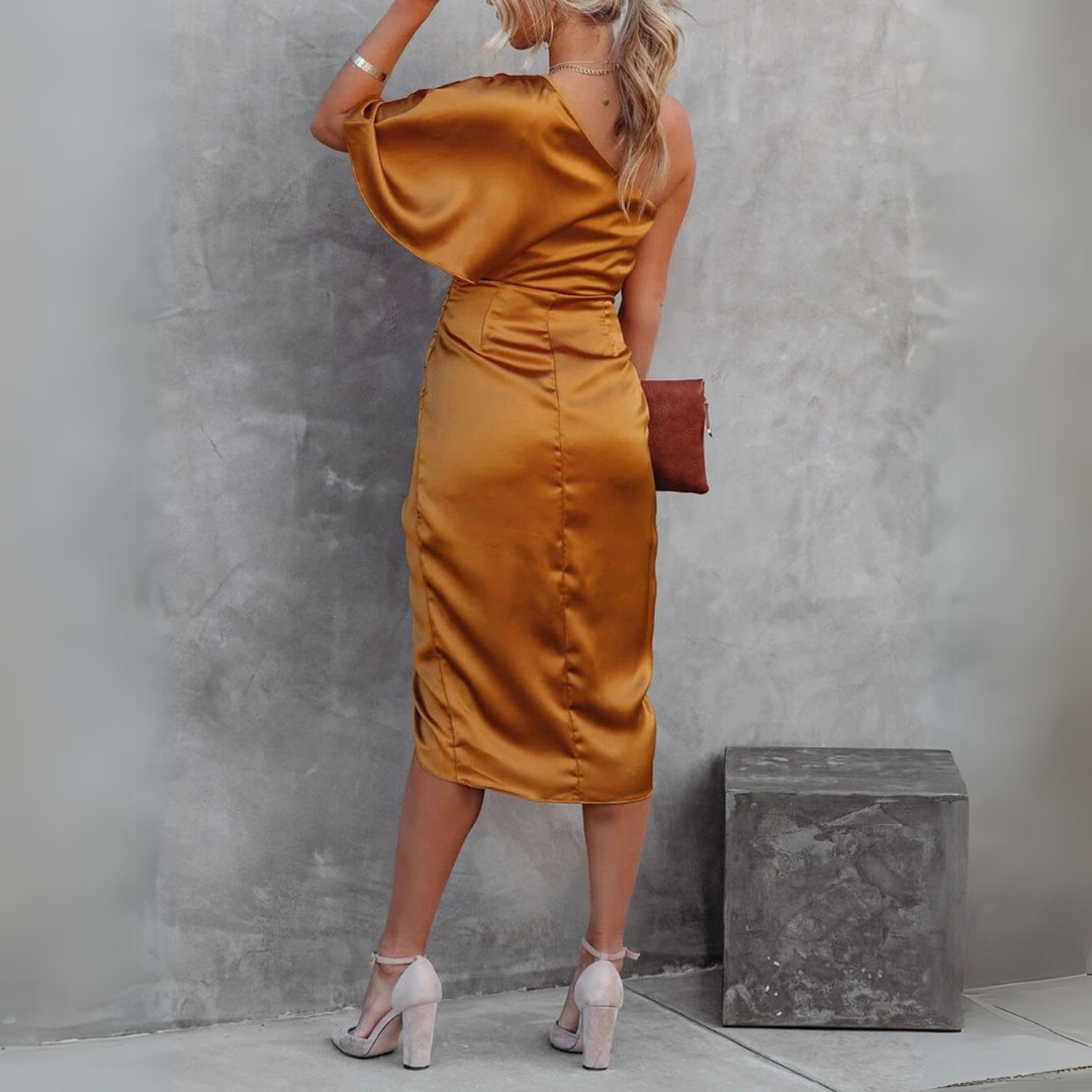 Frau in elegantem, goldfarbenem, schulterfreiem Satinkleid, steht vor grauer Wand, hält braune Clutch, trägt hohe Absätze. Fashion, Abendmode.
