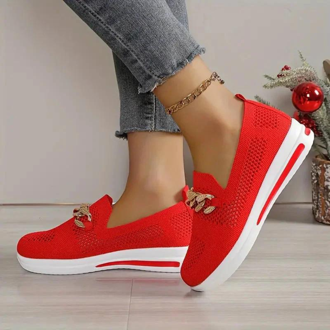 Rote Damen-Sneaker mit weißer Sohle, gestricktem Obermaterial und goldenen Details, getragen mit Jeans. Moderne, bequeme Freizeitschuhe.