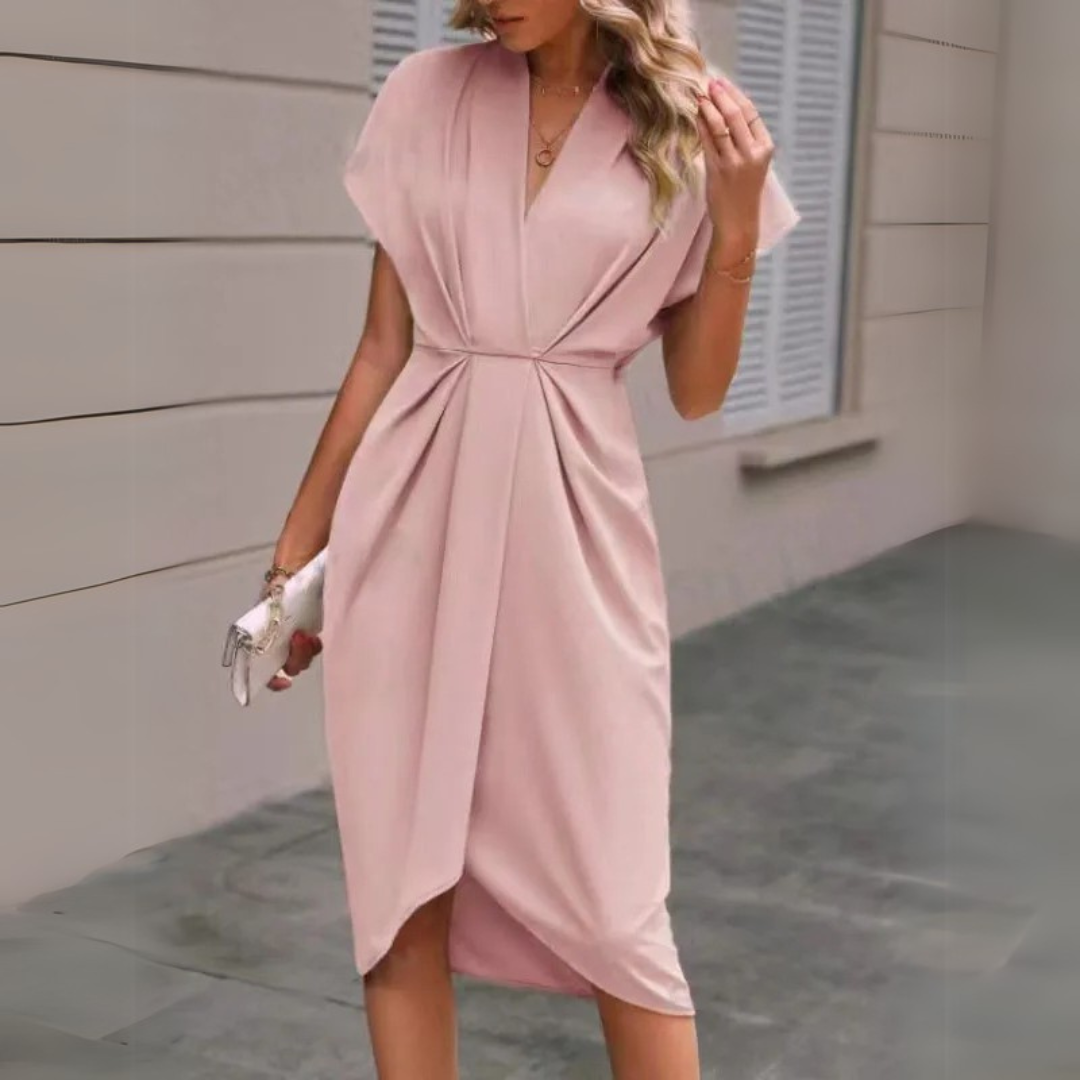 Frau in elegantem, rosa Wickelkleid, steht vor einem modernen Gebäude. Stilvolle Mode, Sommerkleid, schickes Outfit, Damenmode.