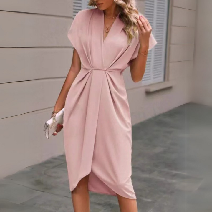 Frau in elegantem, rosa Wickelkleid, steht vor einem modernen Gebäude. Stilvolle Mode, Sommerkleid, schickes Outfit, Damenmode.