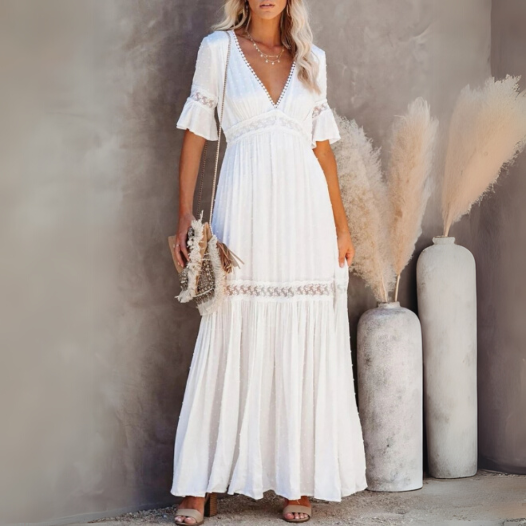 Frau in weißem Boho-Maxikleid mit V-Ausschnitt und Rüschenärmeln, steht neben Pampasgras in Vasen. Sommermode, elegantes Design, Boho-Chic.