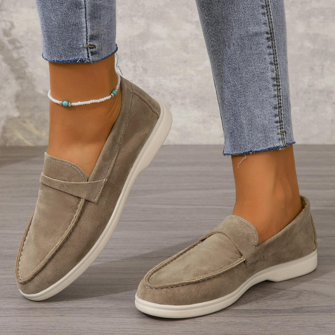 Damenfüße in grauen Wildleder-Loafern, kombiniert mit hellblauen Jeans. Modische, bequeme Schuhe für den Alltag. Eleganter Freizeitlook.