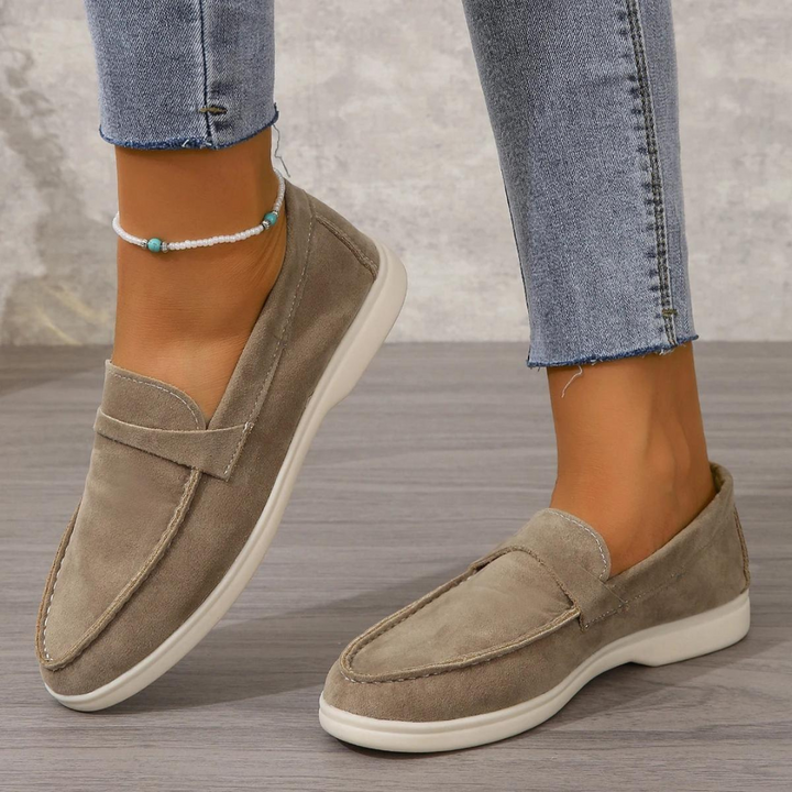 Damenfüße in grauen Wildleder-Loafern, kombiniert mit hellblauen Jeans. Modische, bequeme Schuhe für den Alltag. Eleganter Freizeitlook.