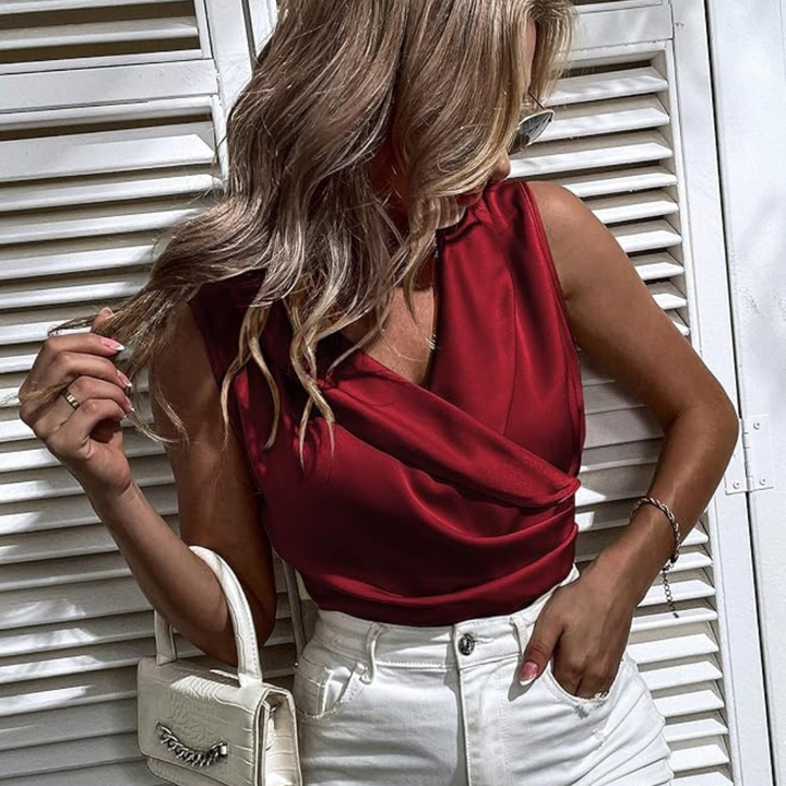 Frau in rotem Satin-Top und weißer Hose vor weißen Fensterläden, hält weiße Handtasche. Elegante Mode, Sommeroutfit, stilvoller Look.