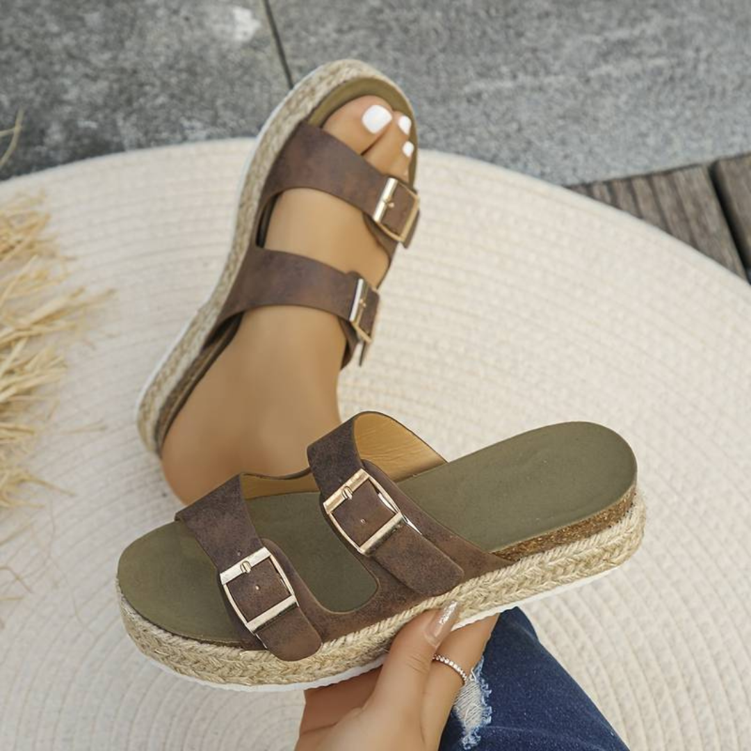 Braune Damen-Sandalen mit doppelten Schnallen und Bastsohle auf hellem Teppich. Modische Sommerschuhe, bequem und stilvoll für Freizeitkleidung.
