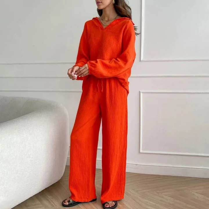 Frau in leuchtend orangefarbenem Freizeitanzug, bestehend aus Hoodie und Hose, steht in modernem Wohnzimmer. Modetrend, bequeme Damenbekleidung.