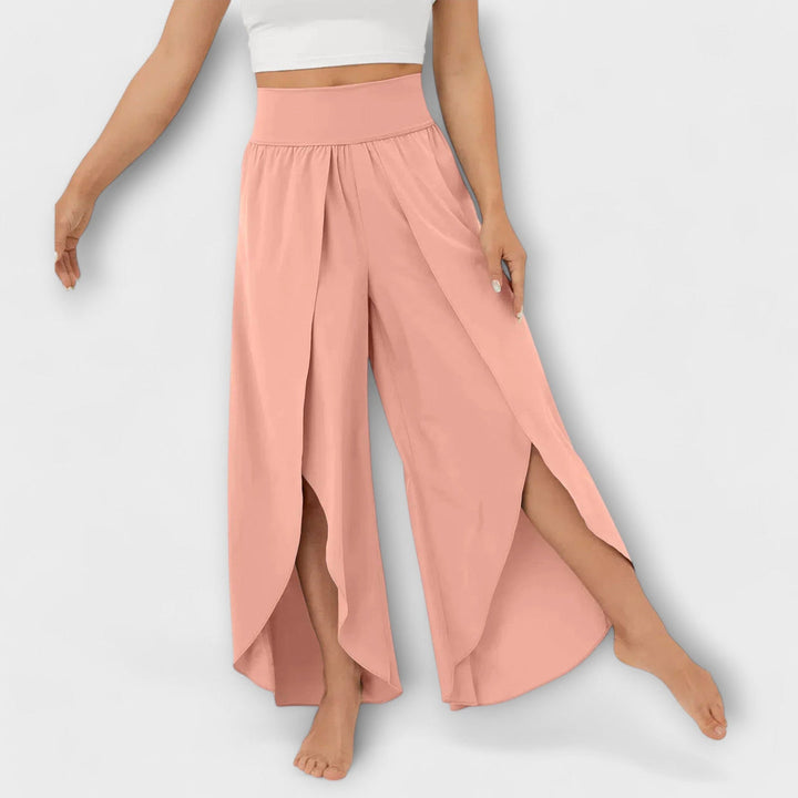 Frau trägt rosa Palazzo-Hose mit hohem Bund und seitlichen Schlitzen, kombiniert mit weißem Crop-Top. Modetrend, Damenbekleidung, Sommeroutfit.