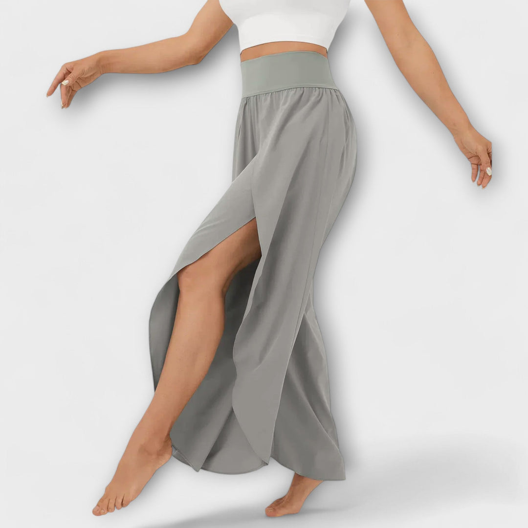 Frau in grauem, fließendem Hosenrock mit hohem Schlitz und elastischem Bund, tanzt barfuß. Elegante Damenmode, bequem und stilvoll.