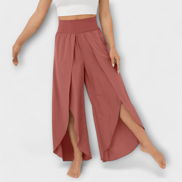 Frau trägt weite, rosafarbene Haremshose mit hohem Bund und seitlichen Schlitzen. Modetrend, Damenbekleidung, bequeme Sommerhose.