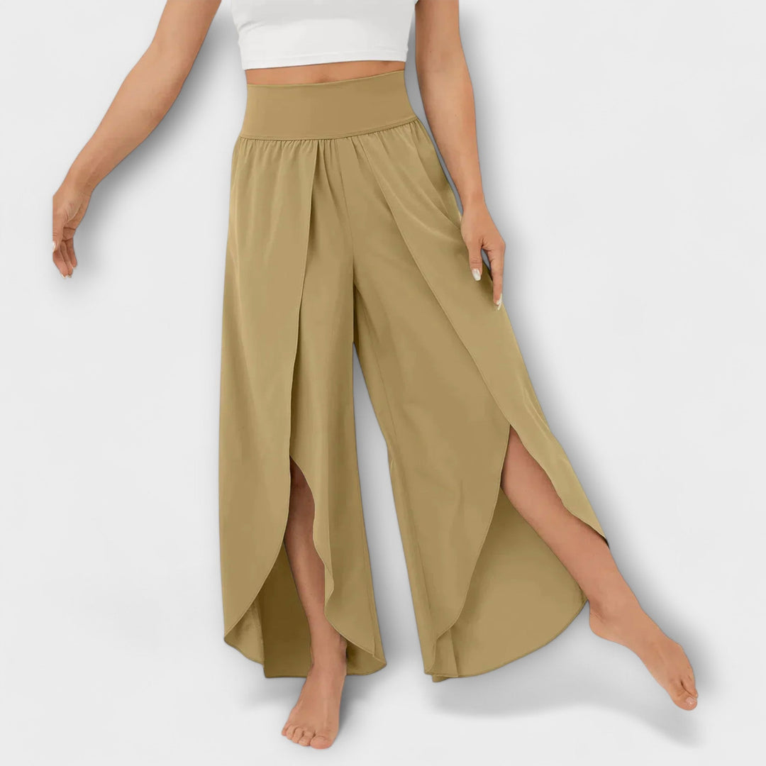 Frau trägt beige, weite Haremshose mit hohem Bund und seitlichen Schlitzen, kombiniert mit weißem Crop-Top. Modetrend, Damenbekleidung, Sommerlook.