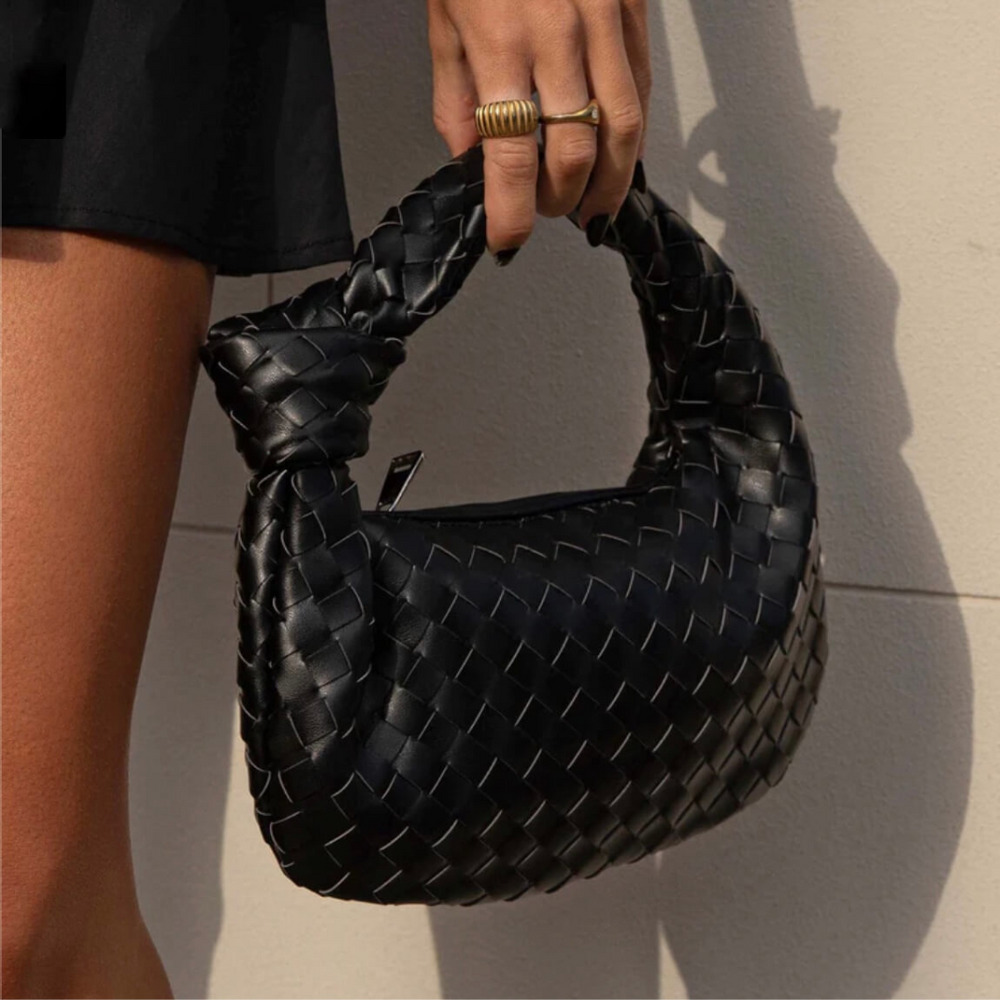 Damenhandtasche aus schwarzem, geflochtenem Leder, getragen von einer Person mit goldenen Ringen. Modische Accessoires, elegantes Design.