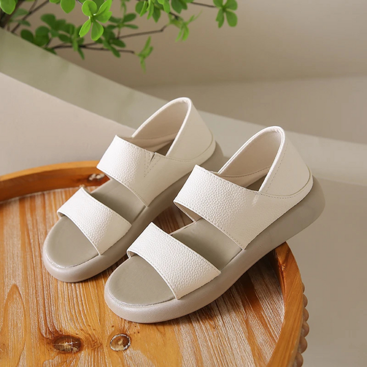 Weiße Sandalen mit zwei Riemen auf einem Holztisch, moderne Sommerschuhe, bequeme Damenmode, minimalistisch, stilvoll, Innenaufnahme.