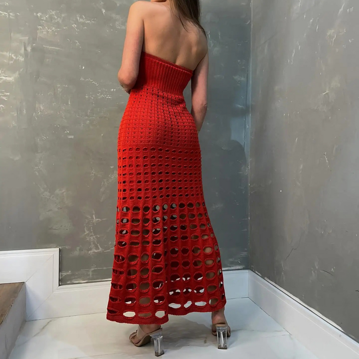 Frau in rotem, schulterfreiem Strickkleid mit Lochmuster, steht in modernem Raum. Elegantes Abendkleid, modische Damenbekleidung, stilvolle Mode.