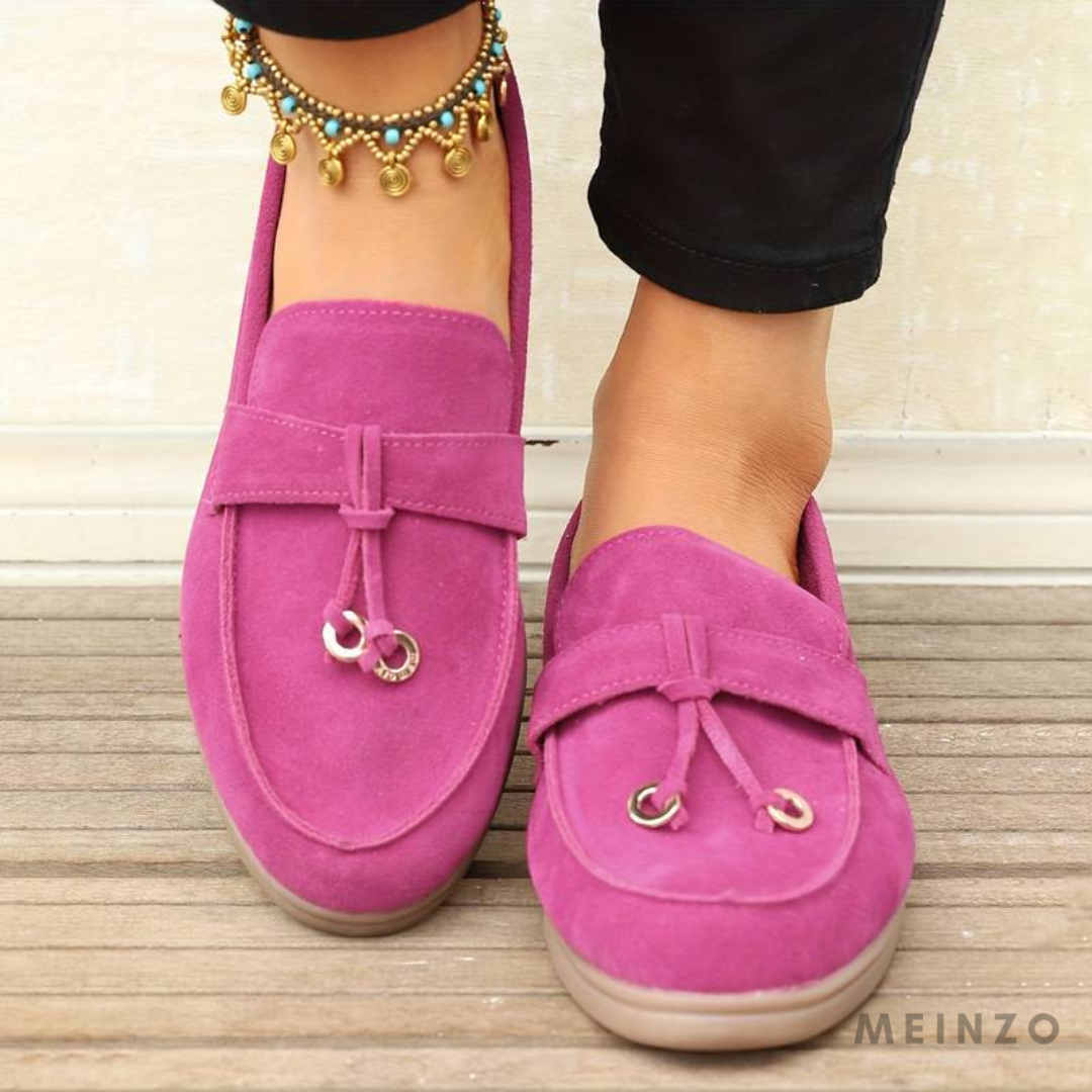 Damen Mokassins in Pink, Wildleder, mit dekorativen Quasten und goldenen Details, getragen auf Holzfußboden. Bequeme, stilvolle Freizeitschuhe.