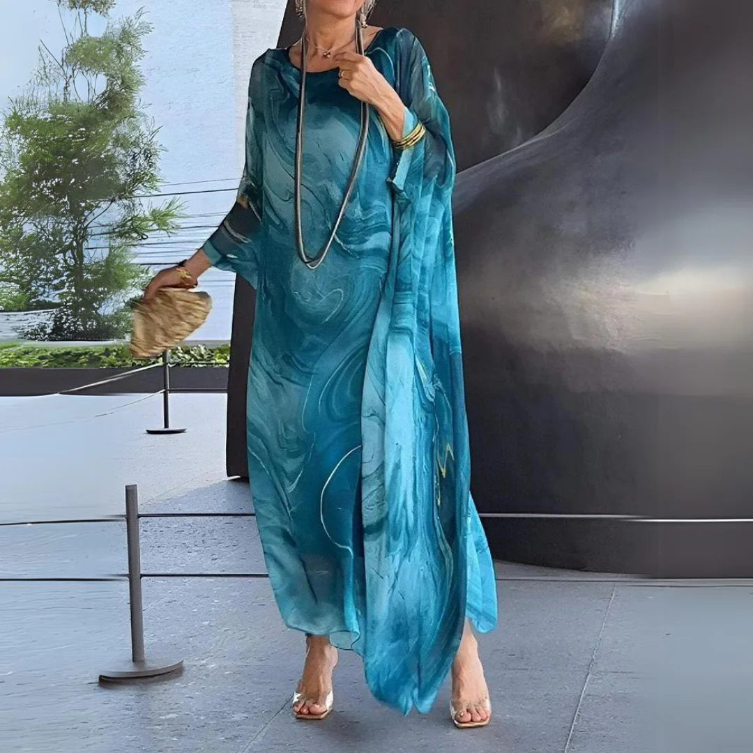 Frau in elegantem, blauem Maxikleid mit abstraktem Muster, goldener Clutch und langen Ketten. Mode, Sommerkleid, Damenbekleidung, stilvoll.