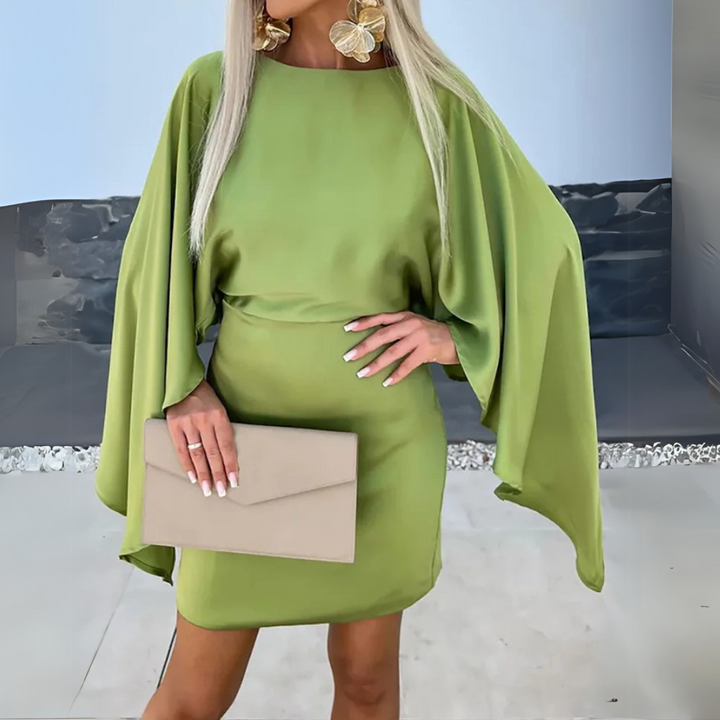 Blonde Frau in grünem Kleid mit Fledermausärmeln, hält beigefarbene Clutch. Elegantes Outfit, Mode, Abendkleid, Accessoires, stilvoll.