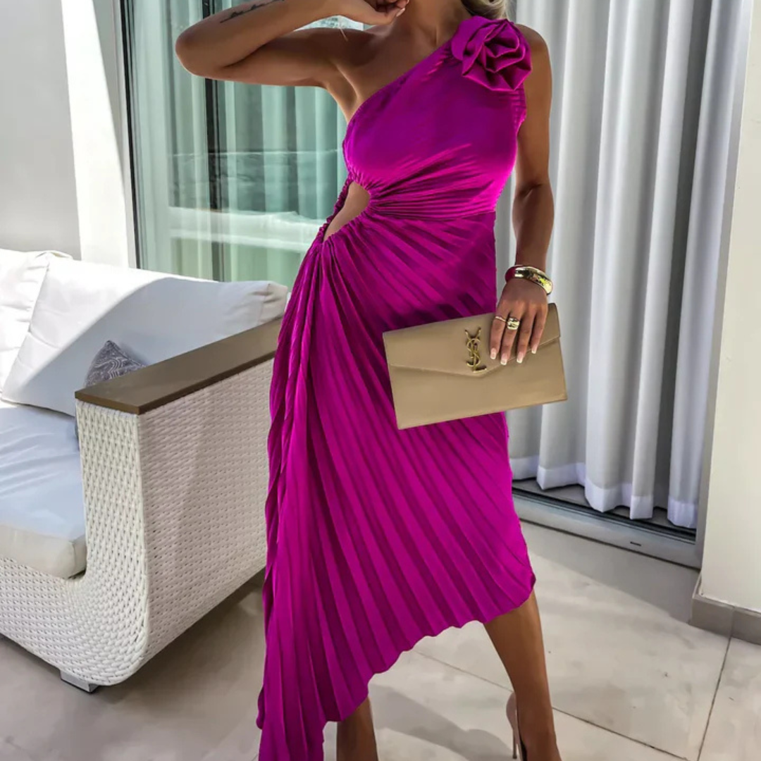 Frau in einem eleganten, einseitigen, fuchsiafarbenen Kleid mit Raffung und Cut-Out, hält eine beige Clutch, steht vor einem modernen Sofa.