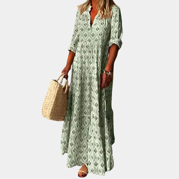 Frau in langem, grünem Maxikleid mit Muster, hält eine geflochtene Strohtasche. Sommermode, elegantes Freizeitoutfit, Damenbekleidung.