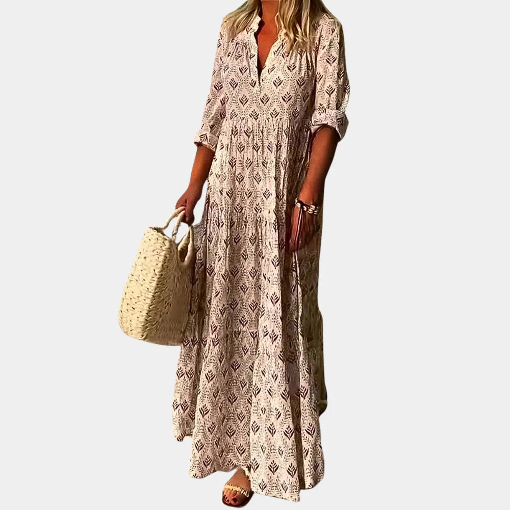 Frau in langem, gemustertem Maxikleid mit V-Ausschnitt und 3/4-Ärmeln, hält eine große, geflochtene Tasche. Sommermode, Damenkleid, Boho-Stil.