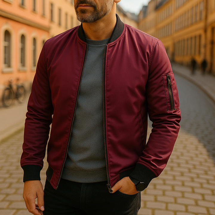 Mann in bordeauxroter Bomberjacke auf gepflasterter Straße, urbane Mode, Herbstoutfit, stilvolle Herrenbekleidung, europäische Stadtarchitektur.