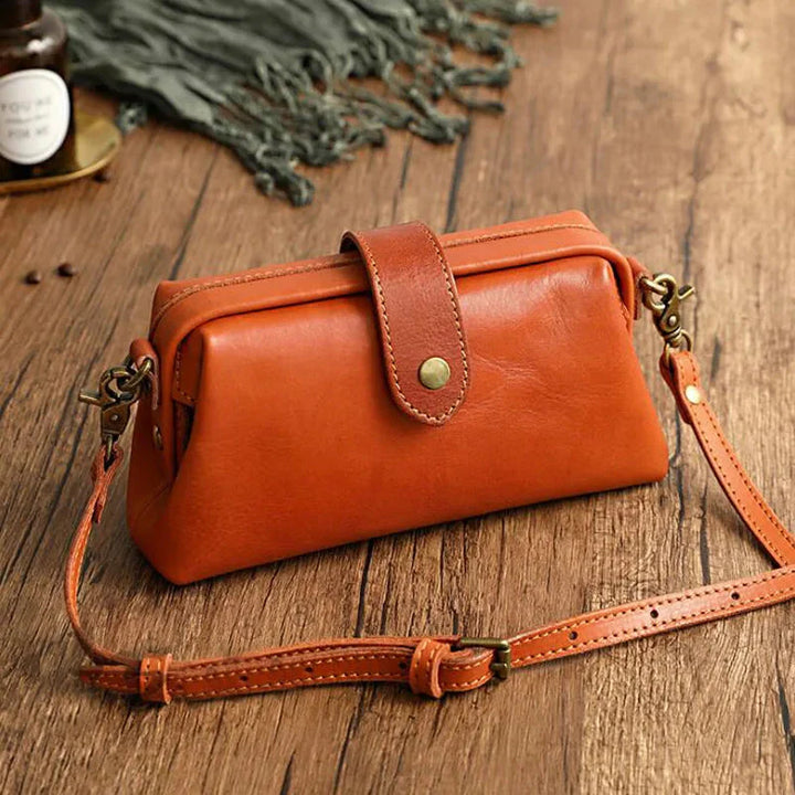 Braune Ledertasche auf Holztisch, Vintage-Design, mit verstellbarem Schulterriemen und Druckknopfverschluss, ideal für stilvolle Aufbewahrung.