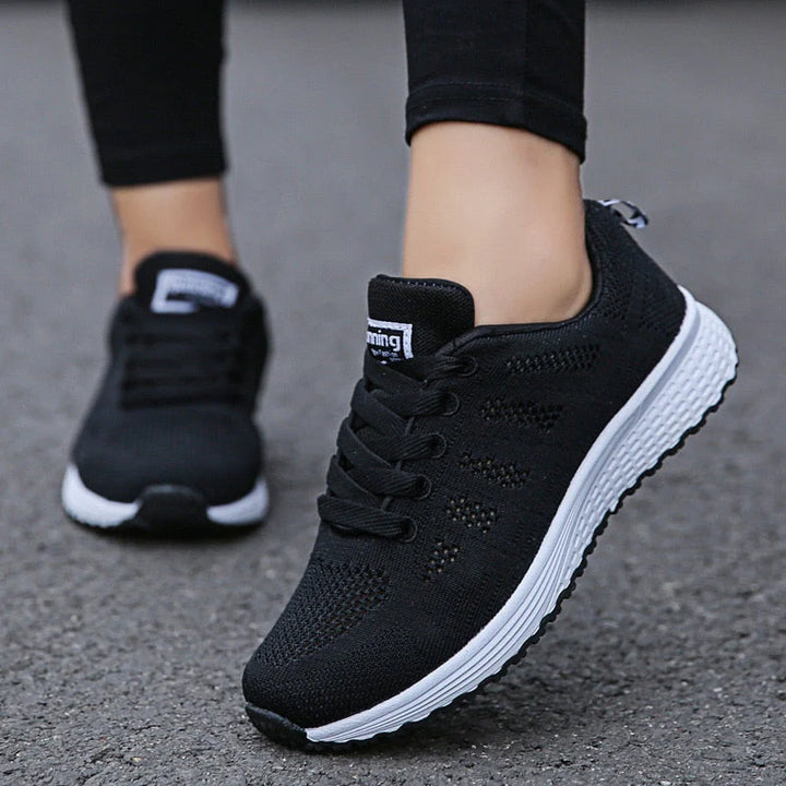 Schwarze Damen-Laufschuhe mit weißer Sohle auf Asphalt, atmungsaktives Mesh-Design, ideal für Sport und Freizeit, modisch und bequem.