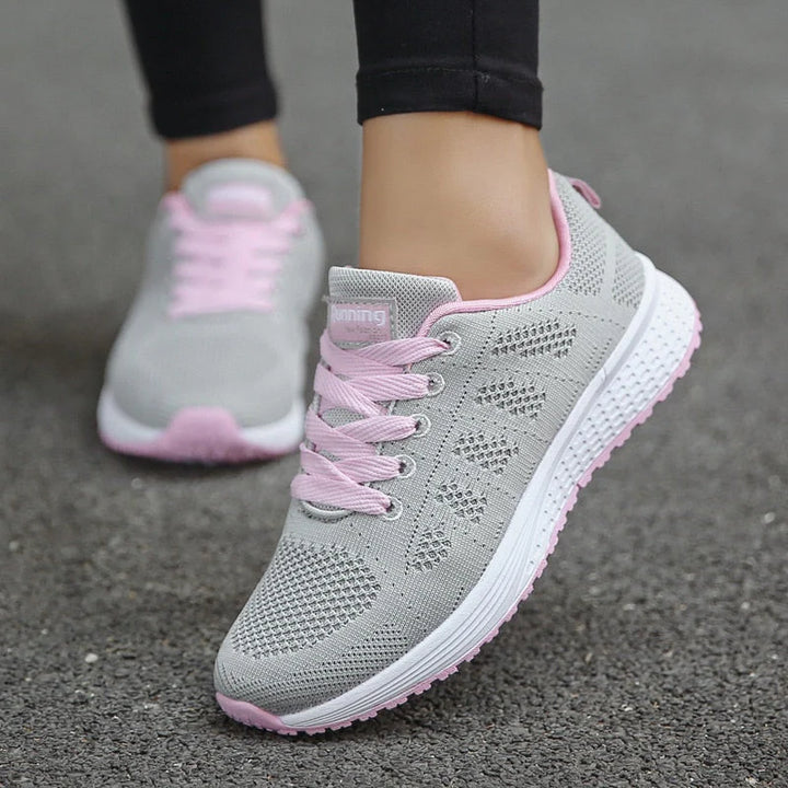 Graue Damen-Laufschuhe mit rosa Schnürsenkeln auf Asphalt. Atmungsaktives Mesh-Design, ideal für Fitness und Sport. Bequeme Sportschuhe.