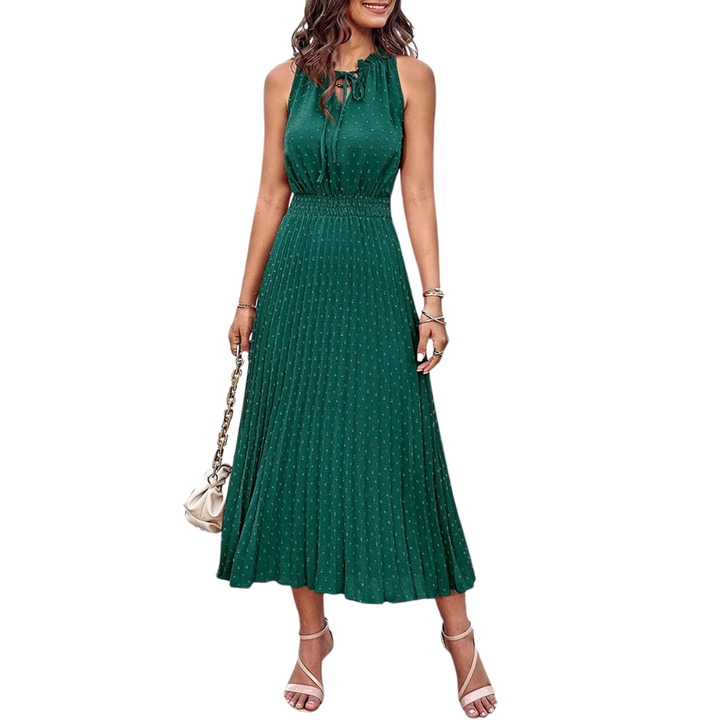 Frau in elegantem, ärmellosem, grünem Sommerkleid mit Plissee-Design, trägt Sandalen und eine Handtasche. Perfekt für stilvolle Sommermode.