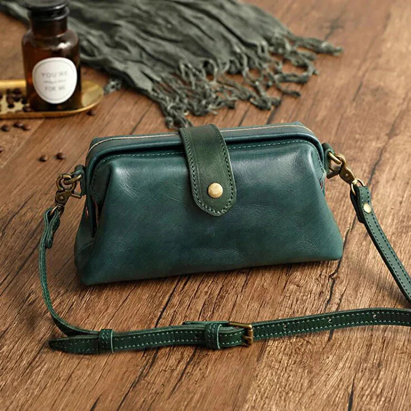Grüne Ledertasche auf Holztisch, Vintage-Stil, mit verstellbarem Schulterriemen und Schnallenverschluss, ideal für Damenmode und Accessoires.
