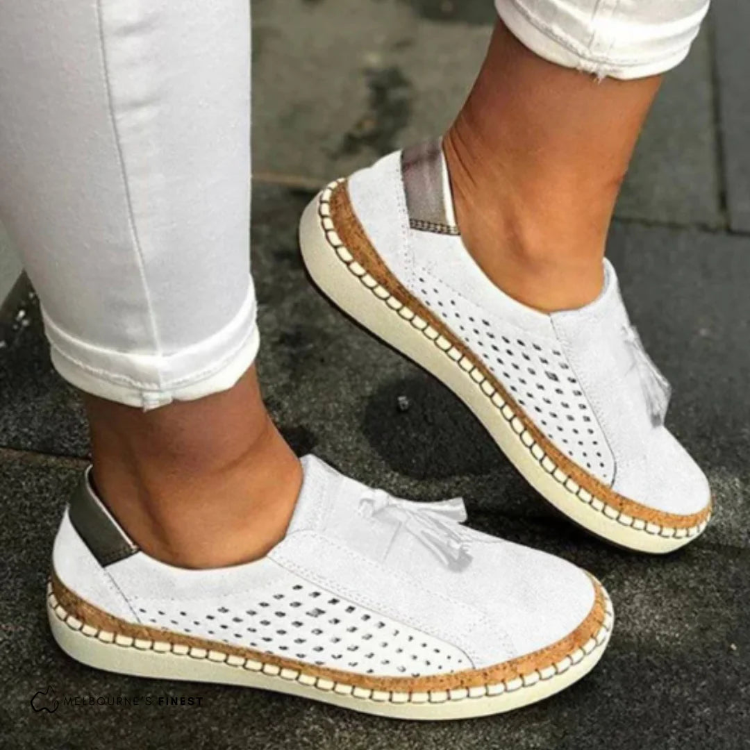 Weiße Damen-Sneaker mit Lochmuster und Korksohle, getragen mit weißen Jeans. Modische, bequeme Schuhe für den Sommer.