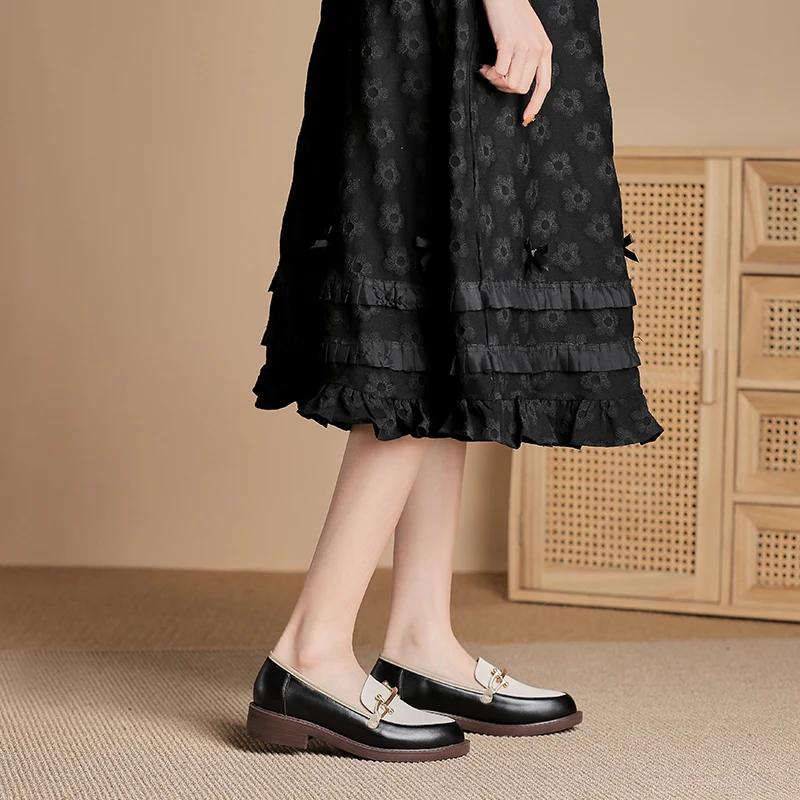 Frau trägt schwarze Loafers mit goldener Schnalle und schwarzem Rock. Modetrend, elegante Schuhe, Damenmode, stilvolle Loafers, Herbstoutfit.