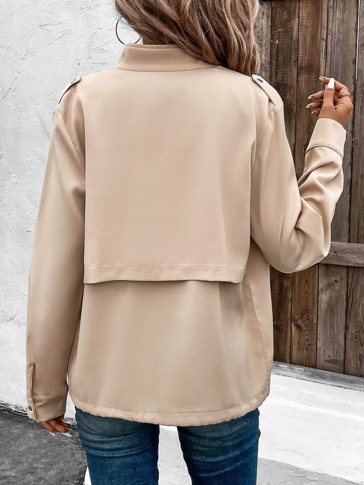 Frau in beiger Jacke und blauer Jeans von hinten, vor Holztür stehend. Modetrend, Herbstmode, Damenbekleidung, lässiger Stil.