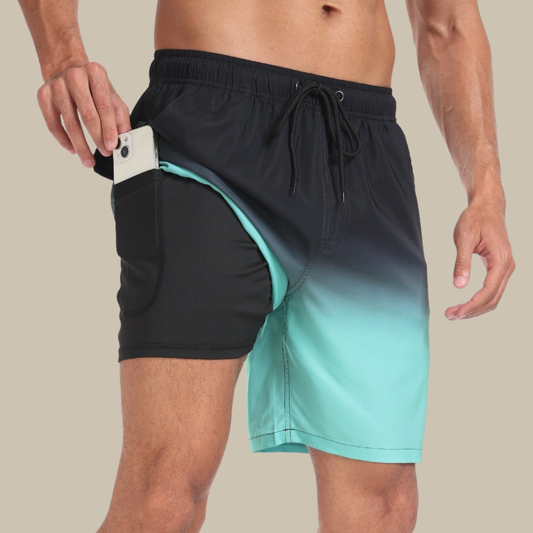 Mann in türkis-schwarzer Badehose mit Handy in der Tasche, zeigt praktische Funktionalität. Ideal für Strand und Sport.