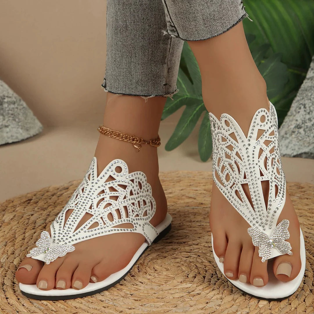 Weiße Sandalen mit Schmetterlingsdesign und Strasssteinen, getragen von einer Person mit Jeans. Elegante Sommerschuhe für Damen.