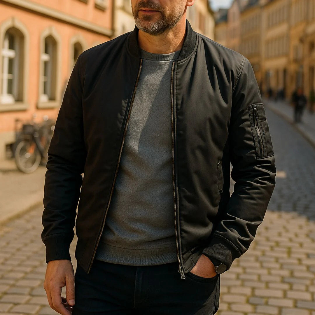 Mann in schwarzer Bomberjacke und grauem Pullover auf gepflasterter Straße in der Stadt. Urbaner Stil, Herrenmode, Herbstbekleidung.