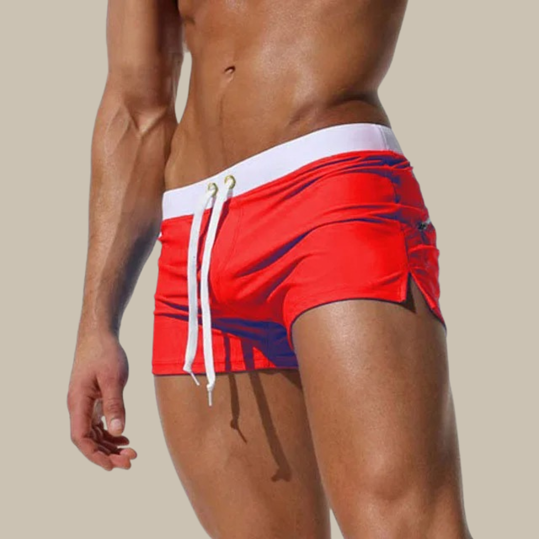 Mann in roter Badehose mit weißem Kordelzug, muskulöser Oberkörper, beige Hintergrund. Sommermode, Herrenbadebekleidung, Strandoutfit.