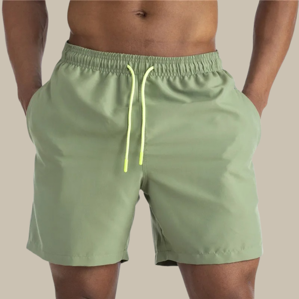 Grüne Herren-Badeshorts mit gelbem Kordelzug, elastischem Bund und Taschen. Ideal für Strand und Schwimmen. Sommermode für Männer.