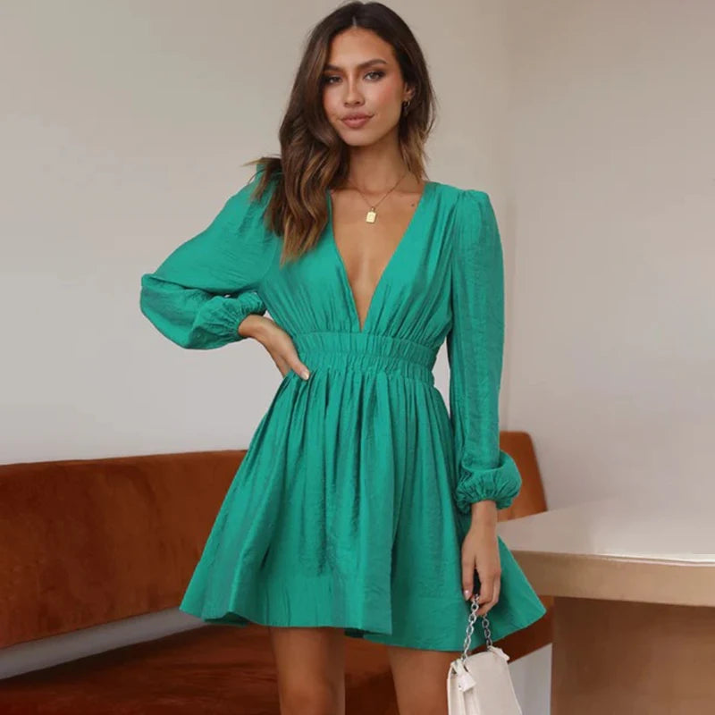 Frau in grünem Kleid mit V-Ausschnitt und langen Ärmeln, steht in modernem Raum. Elegantes Outfit, Mode, Damenbekleidung, stilvoll.