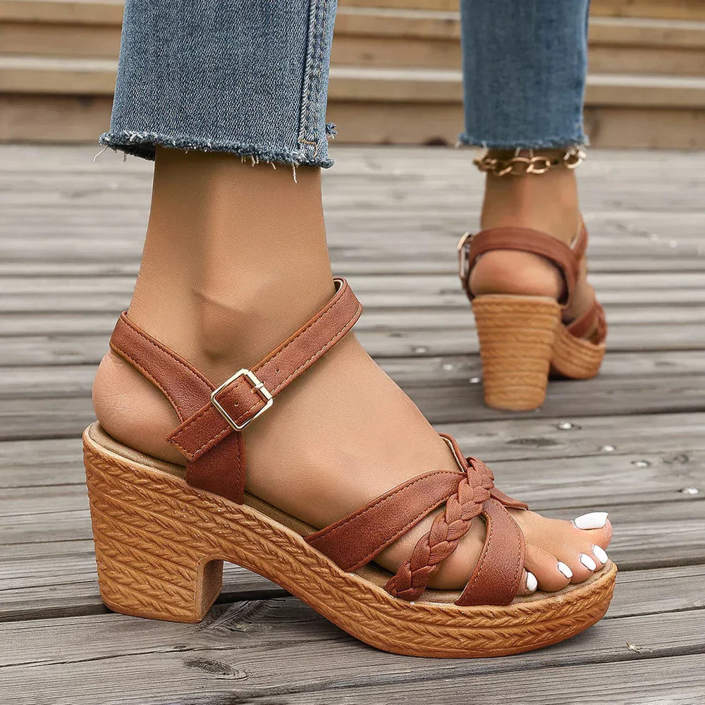 Braune Sandalen mit Keilabsatz und geflochtenem Riemen auf Holzterrasse, getragen mit blauen Jeans. Damenmode, Sommerschuhe, Freizeitlook.
