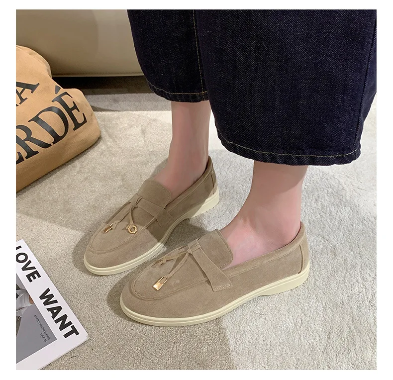 Beige Wildleder-Loafer für Damen auf Teppichboden, kombiniert mit dunklen Jeans. Stilvolle, bequeme Schuhe für Freizeit und Alltag.