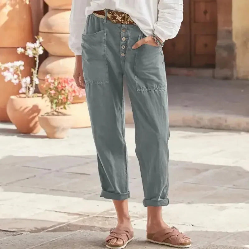 Damen in grauer Leinenhose mit Knopfleiste, weißem Oberteil und Sandalen. Sommermode, lässiger Stil, bequeme Kleidung, Outdoor.