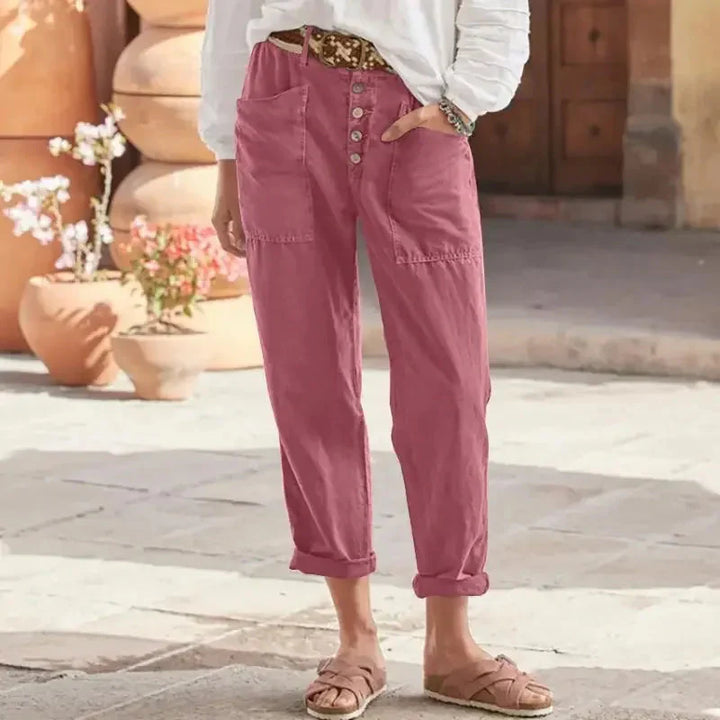 Frau in rosa Leinenhose mit Knopfleiste, weißem Oberteil und Sandalen. Sommermode, lässiger Stil, bequeme Damenbekleidung.