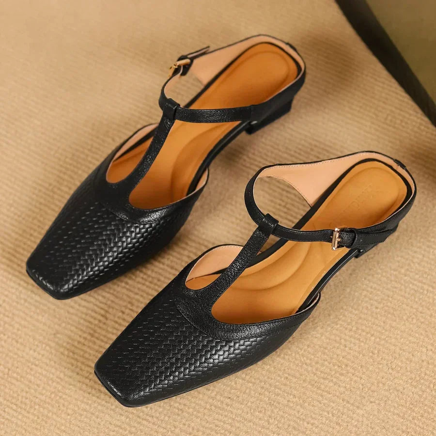 Schwarze Damen-Sandalen mit T-Riemen und quadratischer Spitze auf beigem Teppich. Elegante Sommerschuhe, ideal für modische Outfits.