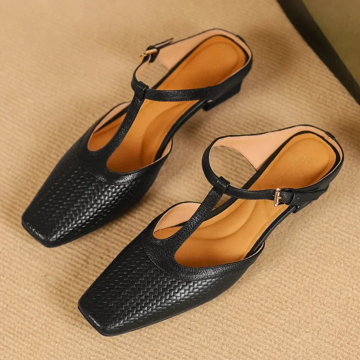 Schwarze Damen-Sandalen mit T-Riemen und quadratischer Spitze auf beigem Teppich. Elegante Sommerschuhe, ideal für modische Outfits.