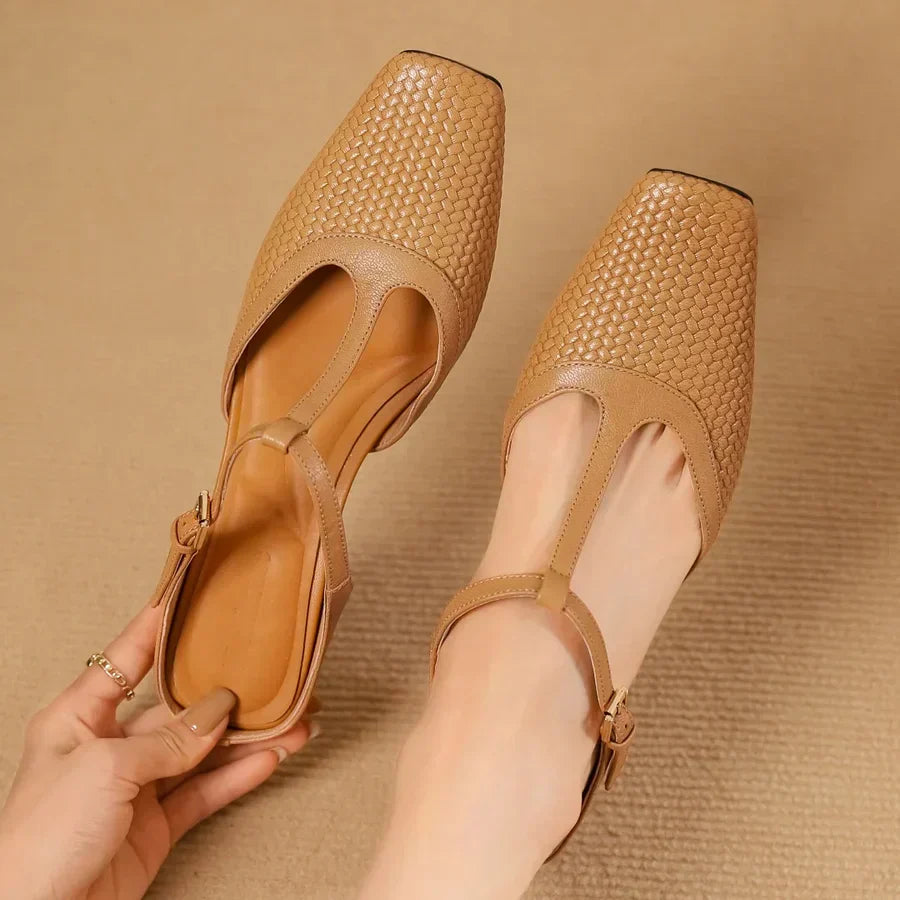 Braune, geflochtene Damen-Sandalen mit T-Riemen und eckiger Spitze auf beigem Hintergrund. Modische Sommerschuhe, elegant und bequem.