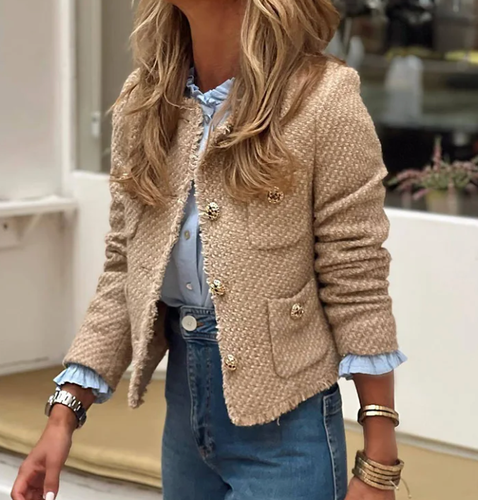 Frau in eleganter, beiger Tweedjacke mit goldenen Knöpfen, blauer Bluse und Jeans. Modetrend, stilvolle Damenbekleidung, Herbstmode.
