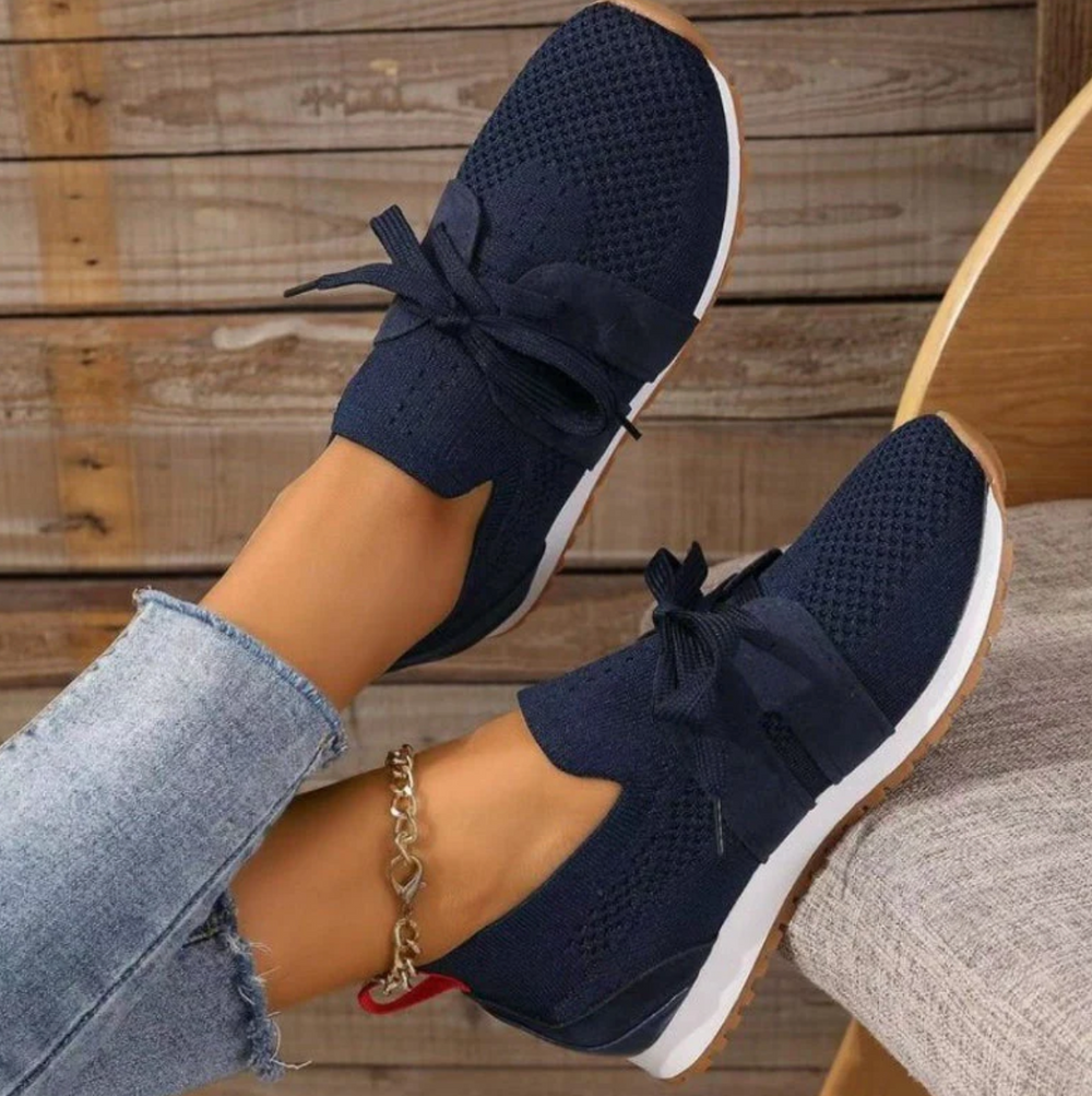 Dunkelblaue Damen-Sneaker mit Schleifen, gestricktem Obermaterial und weißer Sohle, getragen mit Jeans. Bequeme Freizeitschuhe für den Alltag.